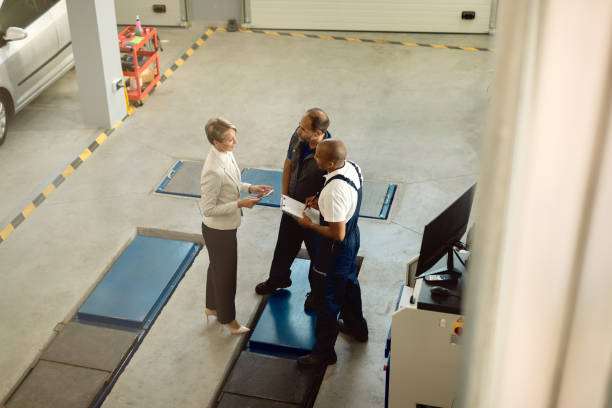Above view of female manager talking to workers in auto repair shop. High angle view of auto mechanics communicating with a businesswoman in a workshop. car mechanic top view stock pictures, royalty-free photos & images