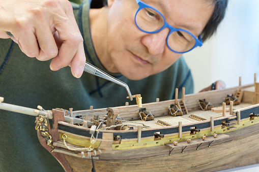 Asian man retirement hobby of wooden model ship building.