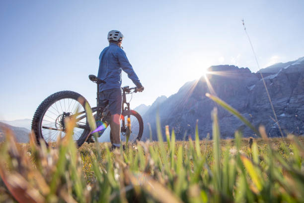 le vététiste de montagne monte à travers le pré alpin au lever du soleil - cycling senior adult sports helmet men photos et images de collection
