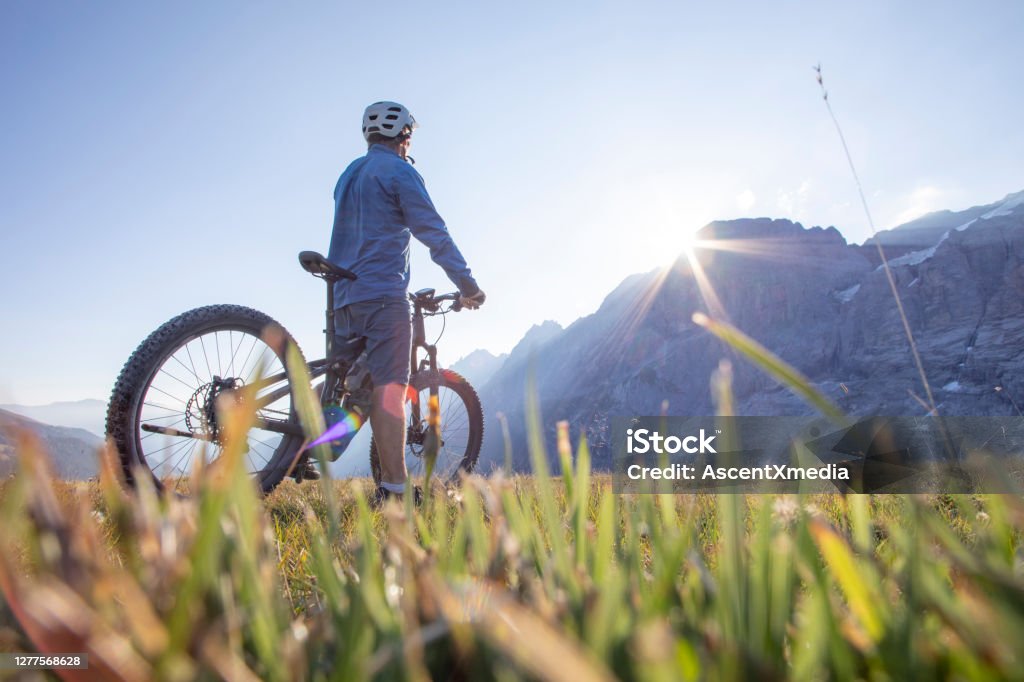 Mountain e-biker rides through alpine meadow at sunrise Swiss Alps in distance Electric Bicycle Stock Photo