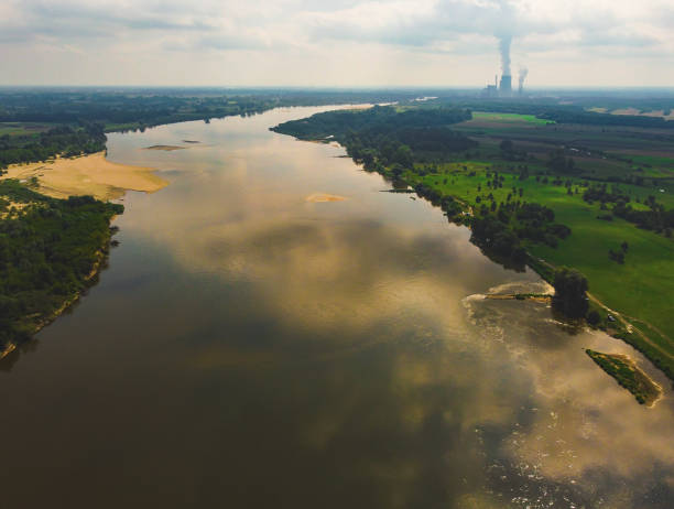 Large river flows through meadows and fields with power plant in a distance. Drone, aerial view stock photo