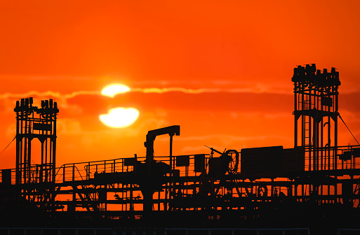 Silhouette pipelines system on crude oil tanker at harbor with blurred sunset sky background