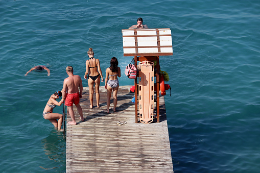 Kusadasi, Turkey​ -​ September 2020: People standing on a wooden pier on a beach of Kusadasi and swimming in a sea, top view