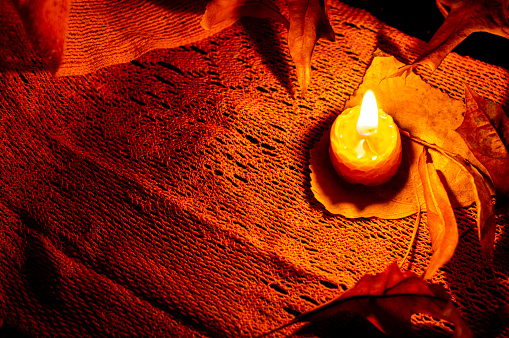 Night time still life of a single bee wax candle and autumn leaves on a orange scarf. Low key