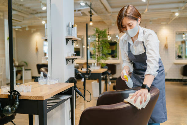 Female hair salon owner wiping down surfaces and disinfecting her shop for reopening A female hair salon owner is wiping down surfaces and disinfecting her shop for reopening. salon cleaning stock pictures, royalty-free photos & images
