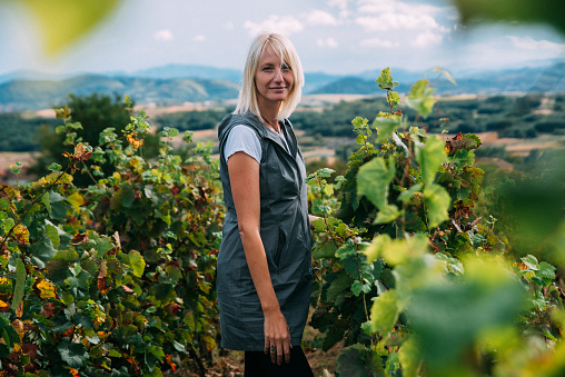Side view of a blond female walking through the vineyard and enjoying on a sunny day in nature with the scenic background