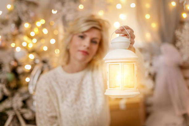 White retro lantern lamp glowing in hand of a mid adult woman in Christmas decoration setting