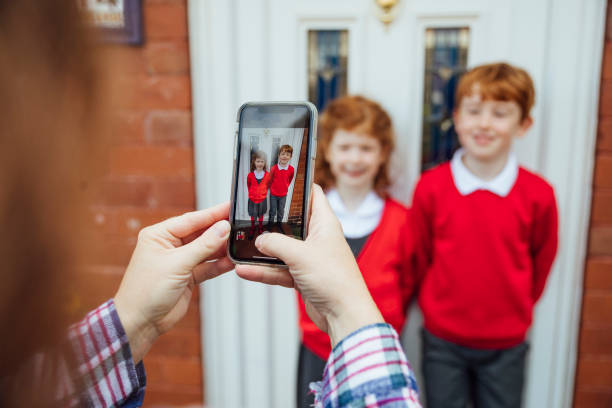 Smile For Mummy! A mother encourages her children to smile for the camera as she takes a picture of them on her mobile phone. back to school photos stock pictures, royalty-free photos & images