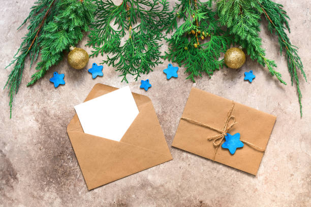 istock Christmas composition. Winter wedding invitation. A blank card in a craft envelope mockup is decorated with green pine branches, balls and blue stars. Beige rustic background. Top view, flat lay. 1277578113