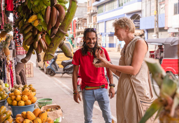ein sri-lankischer mann, ein führer, hilft einer europäischen touristin, 50-jährige aktive frau, frische reife früchte auf einem lokalen straßenmarkt in aluthgama, sri lanka zu pflücken - 30s women asian ethnicity 35 40 years stock-fotos und bilder
