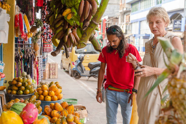 ein mann aus sri lanka hilft einer europäischen touristin, einer 50-jährigen aktiven frau, auf einem lokalen straßenmarkt in aluthgama, sri lanka, frische, reife früchte zu pflücken. - 30s women asian ethnicity 35 40 years stock-fotos und bilder