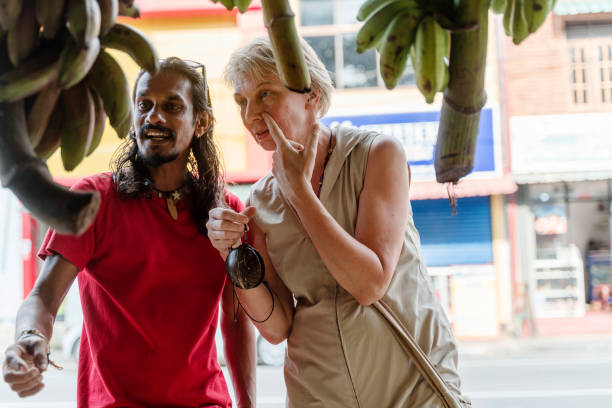 ein sri-lankischer mann, ein führer, hilft einer europäischen touristin, 50-jährige aktive frau, frische reife früchte auf einem lokalen straßenmarkt in aluthgama, sri lanka zu pflücken - 30s women asian ethnicity 35 40 years stock-fotos und bilder