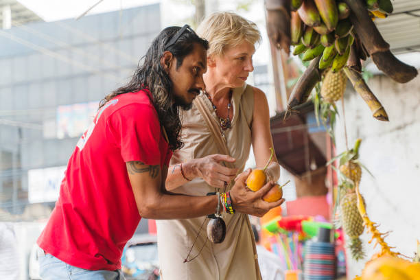 ein sri-lankischer mann, ein führer, hilft einer europäischen touristin, 50-jährige aktive frau, frische reife früchte auf einem lokalen straßenmarkt in aluthgama, sri lanka zu pflücken - 30s women asian ethnicity 35 40 years stock-fotos und bilder