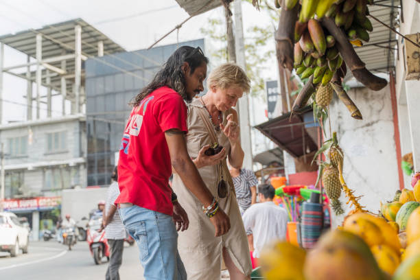 ein sri-lankischer mann, ein führer, hilft einer europäischen touristin, 50-jährige aktive frau, frische reife früchte auf einem lokalen straßenmarkt in aluthgama, sri lanka zu pflücken - 30s women asian ethnicity 35 40 years stock-fotos und bilder