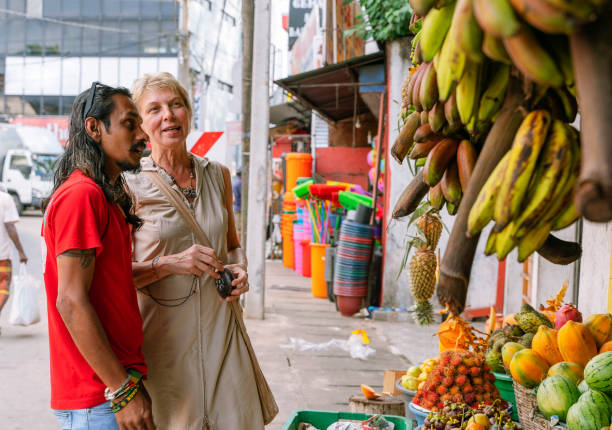 ein sri-lankischer mann, ein führer, hilft einer europäischen touristin, 50-jährige aktive frau, frische reife früchte auf einem lokalen straßenmarkt in aluthgama, sri lanka zu pflücken - 30s women asian ethnicity 35 40 years stock-fotos und bilder