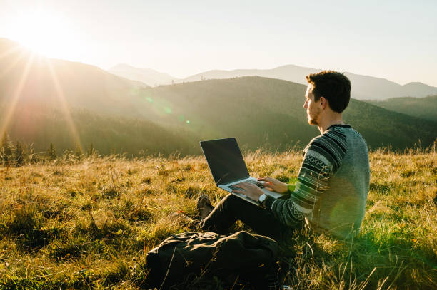 istock Man working outdoors with laptop sitting in mountains. Concept of remote work or freelancer lifestyle. Cellular network broadband coverage. internet 5G. Hiker tourist enjoying valley view sunset. 1277578603