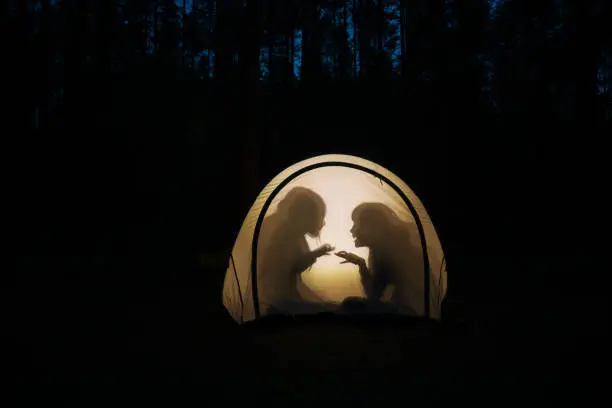 Photo of Children making shadow puppets in a camping tent at night