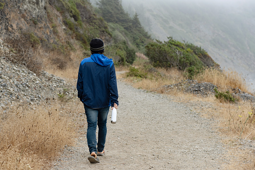 On a cold summer day a Caucasian man in his 30s walks along the hiking trail to Enderts Beach on the coast of California, USA in the Del Norte area of Redwoods National Park.