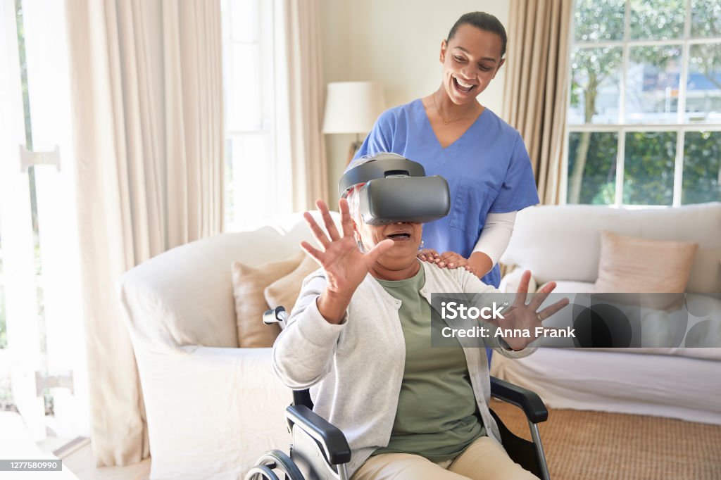 Astonished senior woman with vr glasses Old woman enjoying virtual reality simulator with her elder care nurse Virtual Reality Simulator Stock Photo