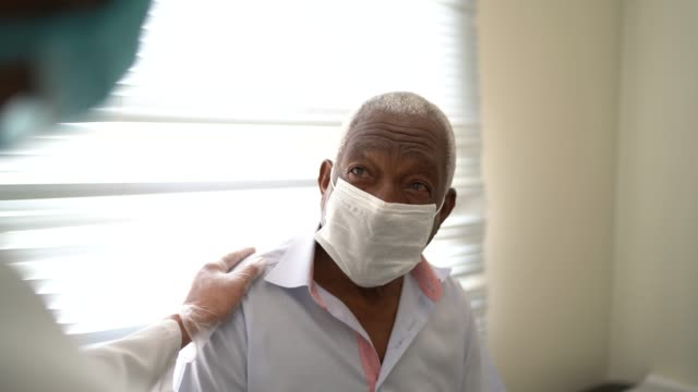 Doctor giving emotional support to a senior patient using face mask