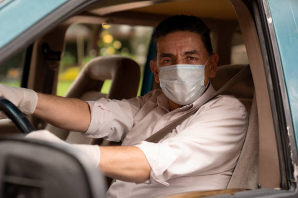 Man wearing a facemask and gloves while driving his car Portrait of a Latin American Man wearing a facemask and gloves while driving his car during the COVID-19 pandemic and looking at the camera car rental covid stock pictures, royalty-free photos & images