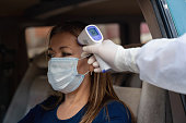 Woman in her car getting her temperature checked with an infrared thermometer during the pandemic