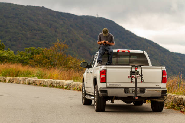 A young man sitting on the ceiling of a Pickup truck sending an SMS Shenandoah Valley, VA, USA, 09/27/2020: A man is inside trunk of a white GMC sierra pickup truck  sitting on the driver cabin playing with his phone. The vehicle is parked at a scenic overlook. skyline drive virginia photos stock pictures, royalty-free photos & images
