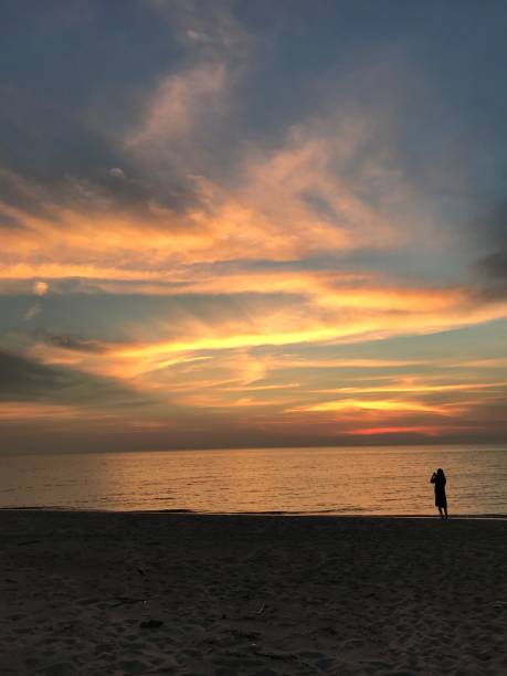istock Woman on beach at sunset, taking a photograph 1277583423