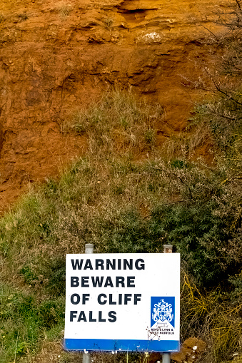 Hunstanton, Norfolk, East Anglia, England, UK. The chalk and sandstone cliffs are constantly being eroded and collapsing on to the beach.  This shows the warning sign beside the beach and in front of the coloured rock strata.