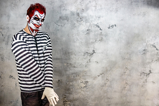 Mid adult man in prisoner costume with red hair and red contact lens imitating a scary shy clown for a Halloween event