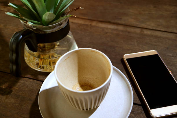 Empty cup of a finished drinking coffee on wooden table with Blank Screen Smartphone and Potted Plant