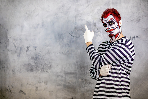 Mid adult man in prisoner costume with red hair and red contact lens imitating a scary  angry clown for a Halloween event