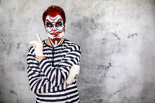 Mid adult man in prisoner costume with red hair and red contact lens imitating a scary  pensive clown for a Halloween event