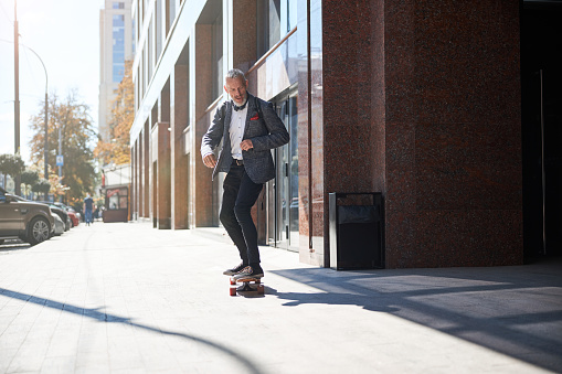 Energetic senior man riding a longboard in the street and enjoying life