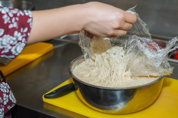 istock Pulling the plastic wrap off the raised bread dough in a metal mixing bowl. The gluten is stretched, showing that the raw flour mixture can be formed into a loaf and baked. 1277589502