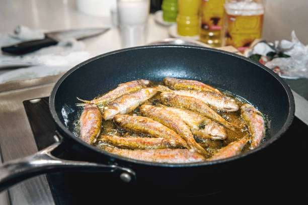 el pescado pequeño de barábulo y caballa se fríe en aceite en una sartén en una olla de inducción - poco profundo fotografías e imágenes de stock