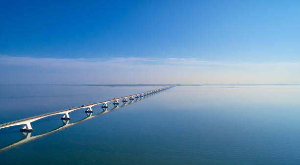 Zeeland Bridge aerial The Zeelandbrug during sunrise. The Sky is blue and it’s reflected in the water of the North sea. The bridge is also reflected in the water. Cars drive at a high speed over it. netherlands aerial stock pictures, royalty-free photos & images