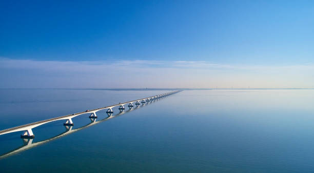 Zeeland Bridge aerial The Zeelandbrug during sunrise. The Sky is blue and it’s reflected in the water of the North sea. The bridge is also reflected in the water. Cars drive at a high speed over it. sea bridge stock pictures, royalty-free photos & images