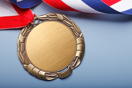 A blank gold medal attached to a red white and blue ribbon on a blue background.