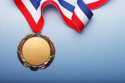 A blank gold medal attached to a red white and blue ribbon on a blue background.