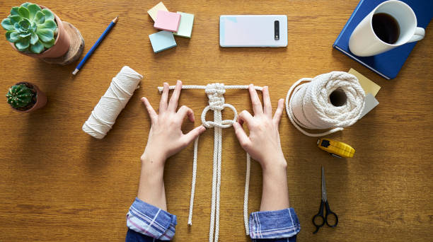 A young woman working on macrame decor with tools over a creative desktop at home A young woman working on macrame decor with tools over a creative desktop at home watched from above macrame photos stock pictures, royalty-free photos & images