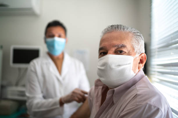 얼굴 마스크를 사용하여 환자의 팔에 백신을 적용하는 간호사의 초상화 - doctor male doctor mature men portrait 뉴스 사진 이미지