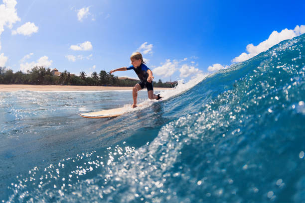 les jeunes surfeurs apprennent à monter sur la planche de surf sur les vagues de mer - exercising wetsuit people expressing positivity photos et images de collection