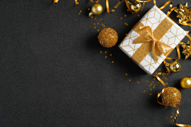 istock Christmas flat lay composition. Luxury gift box, golden balls and decorations on black background. Top view with copy space. Xmas banner template, New Year greeting card mockup. 1277604653