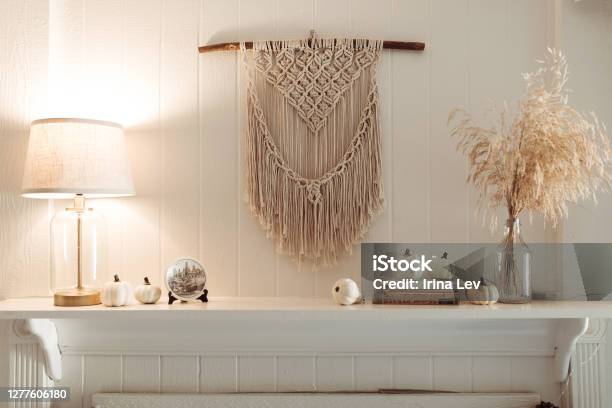 Thanksgiving Home Decor White Wooden Fireplace With Wall Macrame Cream And Beige Pumpkins Pine Cones Garland And Rustic Dry Wheat Bouquet House Fall Decoration Stock Photo - Download Image Now