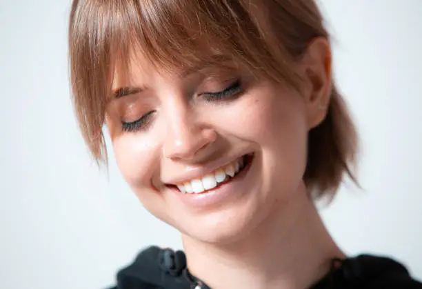 Photo of Close up portrait of young pretty girl with closed eyes, white toothy smile and healthy skin. Human emotions language