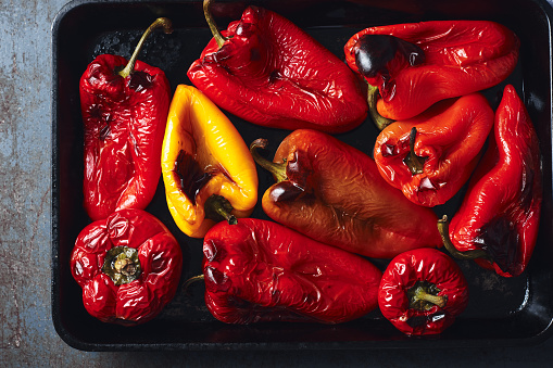 Roasted red and yellow peppers in baking tray on a dark background. Top view.