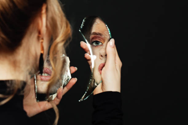 istock Serious woman looking at broken self-image mirror on black background 1277611948