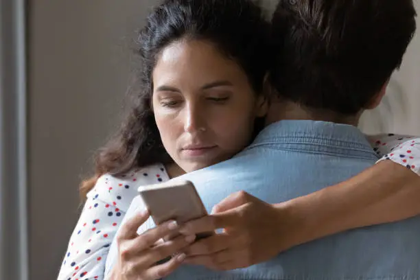 Photo of Young woman hug husband cheating online on cellphone