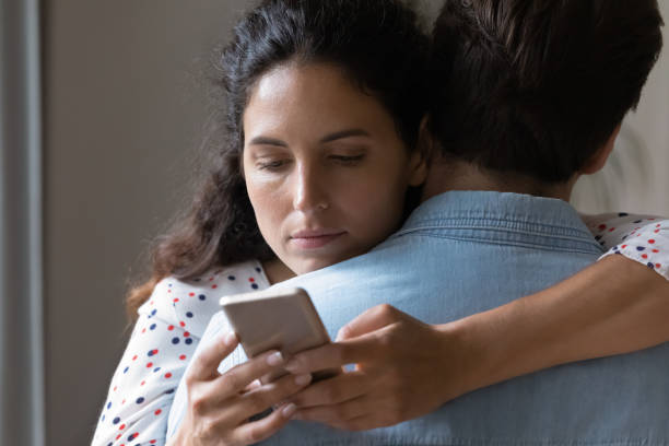 young woman hug husband cheating online on cellphone - infidelidade imagens e fotografias de stock